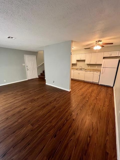Unfurnished living room with a textured ceiling, dark wood-style floors, a ceiling fan, and stairway
