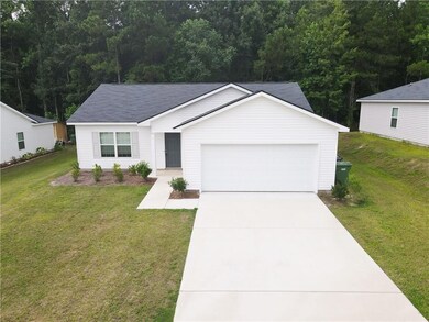 Ranch-style home with a garage, concrete driveway, a front lawn, and a view of trees