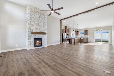 Unfurnished living room with ceiling fan, a chandelier, a stone fireplace, high vaulted ceiling, and dark wood finished floors