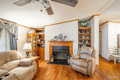 Living area featuring a textured ceiling, ornamental molding, a glass covered fireplace, light wood-style floors, and ceiling fan