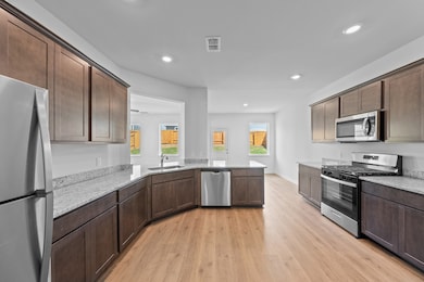 Kitchen featuring appliances with stainless steel finishes, light stone countertops, light wood-style floors, dark brown cabinets, and recessed lighting
