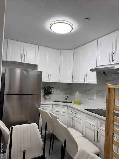 Kitchen with white cabinetry, refrigerator, light stone counters, exhaust hood, and backsplash