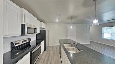 Kitchen with stainless steel appliances, tasteful backsplash, light wood-type flooring, white cabinets, and dark stone counters