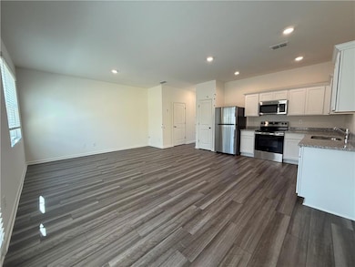 Kitchen with stainless steel appliances, a sink, white cabinets, dark wood-type flooring, and light stone counters