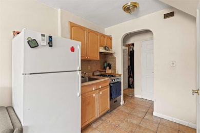 Kitchen featuring freestanding refrigerator, gas stove, decorative backsplash, arched walkways, and light tile patterned flooring