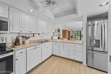 Kitchen with stainless steel appliances, recessed lighting, a raised ceiling, a sink, and light wood-type flooring
