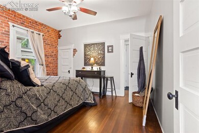 Bedroom with dark wood-style floors, brick wall, baseboards, and a ceiling fan
