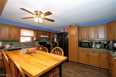 Kitchen with dark wood finished floors, black appliances, brown cabinetry, and light countertops