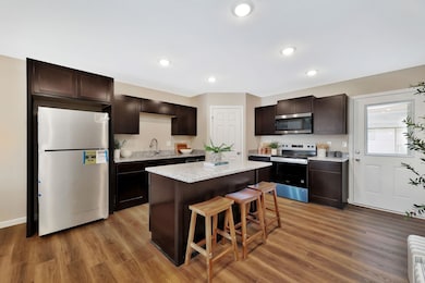 Kitchen featuring stainless steel appliances, dark brown cabinets, a kitchen breakfast bar, light wood finished floors, and recessed lighting