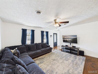 Living room with a textured ceiling, dark wood-style flooring, and ceiling fan