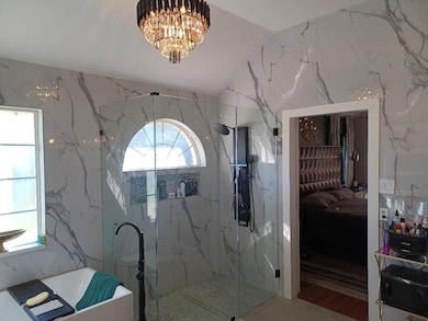 Full bathroom featuring stone wall, connected bathroom, a freestanding tub, a chandelier, and tile walls