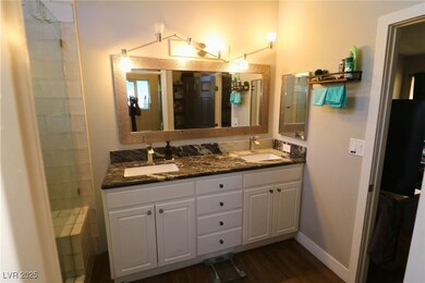 Bathroom featuring double vanity, dark wood-style floors, and tiled shower