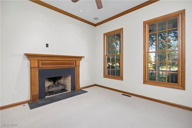 Unfurnished living room featuring carpet flooring, ornamental molding, a ceiling fan, plenty of natural light, and a fireplace with flush hearth