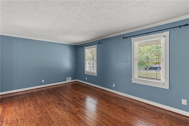Unfurnished room featuring ornamental molding, healthy amount of natural light, dark wood-style floors, and a textured ceiling
