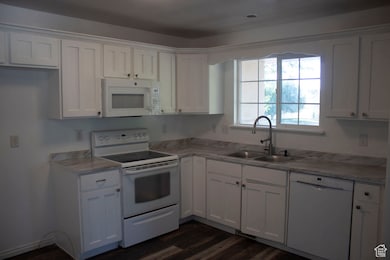 Kitchen featuring white appliances, white cabinetry, light countertops, and dark wood-style flooring
