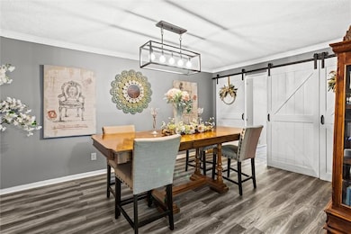 Dining room featuring dark wood-type flooring, a barn door, and crown molding