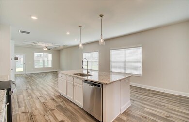 Kitchen featuring stainless steel dishwasher, a center island with sink, light stone counters, recessed lighting, and white cabinets