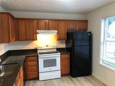 Kitchen featuring white range with electric stovetop, freestanding refrigerator, under cabinet range hood, brown cabinets, and a textured ceiling