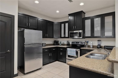 Kitchen featuring appliances with stainless steel finishes, light tile patterned floors, dark cabinetry, and a sink