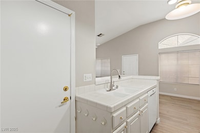 Kitchen featuring tile countertops, light wood-type flooring, lofted ceiling, white cabinetry, and white dishwasher
