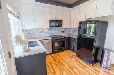 Kitchen featuring black appliances, backsplash, light wood-type flooring, white cabinetry, and light stone counters