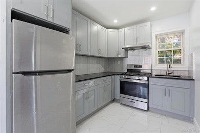 Kitchen with appliances with stainless steel finishes, light marble finish floors, gray cabinetry, decorative backsplash, and under cabinet range hood