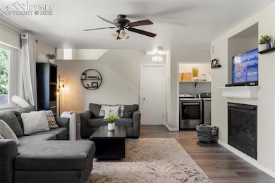 Living area featuring washing machine and dryer, a ceiling fan, wood finished floors, and a glass covered fireplace