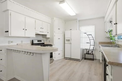 Kitchen featuring a peninsula, white fridge with ice dispenser, stainless steel gas range oven, light countertops, and white cabinets