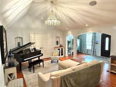 Living area with wood finished floors, a chandelier, arched walkways, vaulted ceiling, and recessed lighting