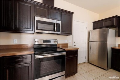 Kitchen with stainless steel appliances, light tile patterned flooring, dark brown cabinets, and dark countertops