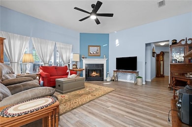 Living area with a tile fireplace, light wood-style flooring, a ceiling fan, and a textured ceiling