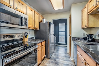 This kitchen features modern stainless steel appliances, wooden cabinetry, and a sleek black countertop. It has a compact galley layout with a window providing natural light.