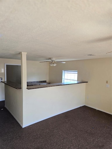 Empty room featuring dark carpet, a ceiling fan, and a textured ceiling