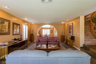 Carpeted living area with stairs and arched walkwa