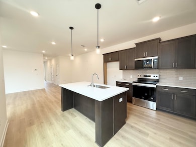 Kitchen featuring stainless steel appliances, a sink, light wood-type flooring, backsplash, and light countertops
