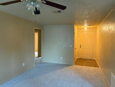 Carpeted empty room featuring a textured ceiling, ceiling fan, and baseboards