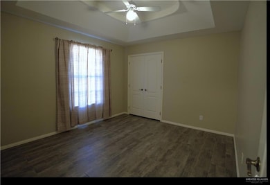 Empty room featuring a raised ceiling, dark wood-style floors, and ceiling fan
