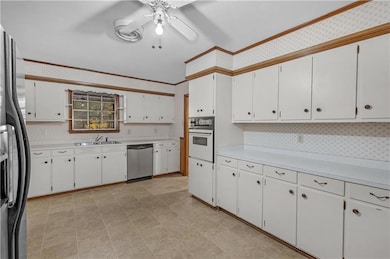Kitchen with light countertops, white cabinets, appliances with stainless steel finishes, crown molding, and wallpapered walls
