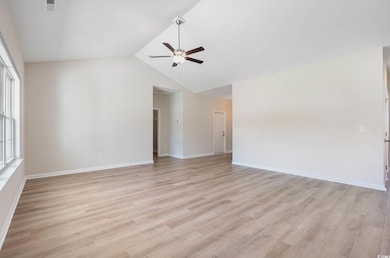 Unfurnished living room with a ceiling fan, vaulted ceiling, light wood finished floors, and baseboards