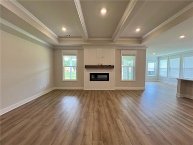 Unfurnished living room featuring plenty of natural light, ornamental molding, a glass covered fireplace, dark wood-type flooring, and baseboards