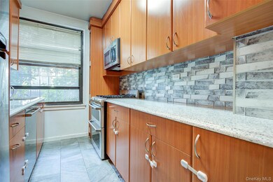Kitchen with decorative backsplash, light stone countertops, stainless steel appliances, brown cabinetry, and light tile patterned floors