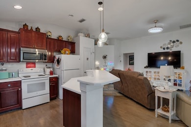Kitchen with white appliances, light countertops, hanging light fixtures, a kitchen island, and vaulted ceiling
