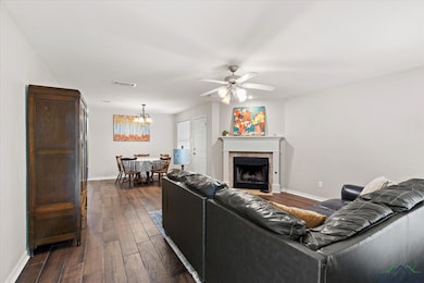 Living area with dark wood-type flooring, ceiling fan, a chandelier, and a fireplace