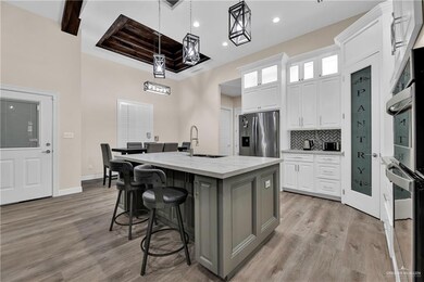 Kitchen with light wood finished floors, tasteful backsplash, a center island with sink, white cabinetry, and stainless steel refrigerator with ice dispenser