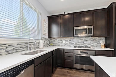 Kitchen with appliances with stainless steel finishes, dark brown cabinets, dark wood-style floors, light stone countertops, and decorative backsplash