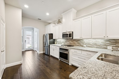 Kitchen featuring appliances with stainless steel finishes, arched walkways, decorative backsplash, white cabinets, and recessed lighting