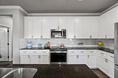 Kitchen featuring crown molding, stainless steel appliances, white cabinetry, decorative backsplash, and dark stone counters
