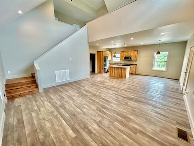 Unfurnished living room featuring stairs, recessed lighting, light wood finished floors, and a towering ceiling