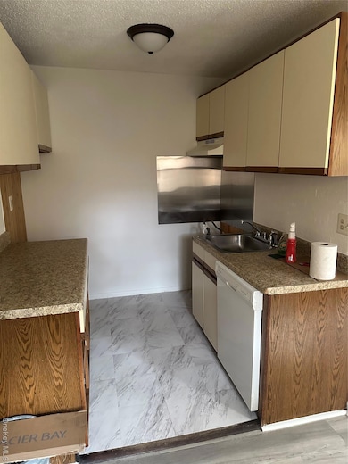 Kitchen with a textured ceiling, dishwasher, extractor fan, dark countertops, and cream cabinetry