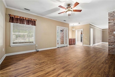 Unfurnished living room featuring a ceiling fan, wood finished floors, baseboards, and ornamental molding